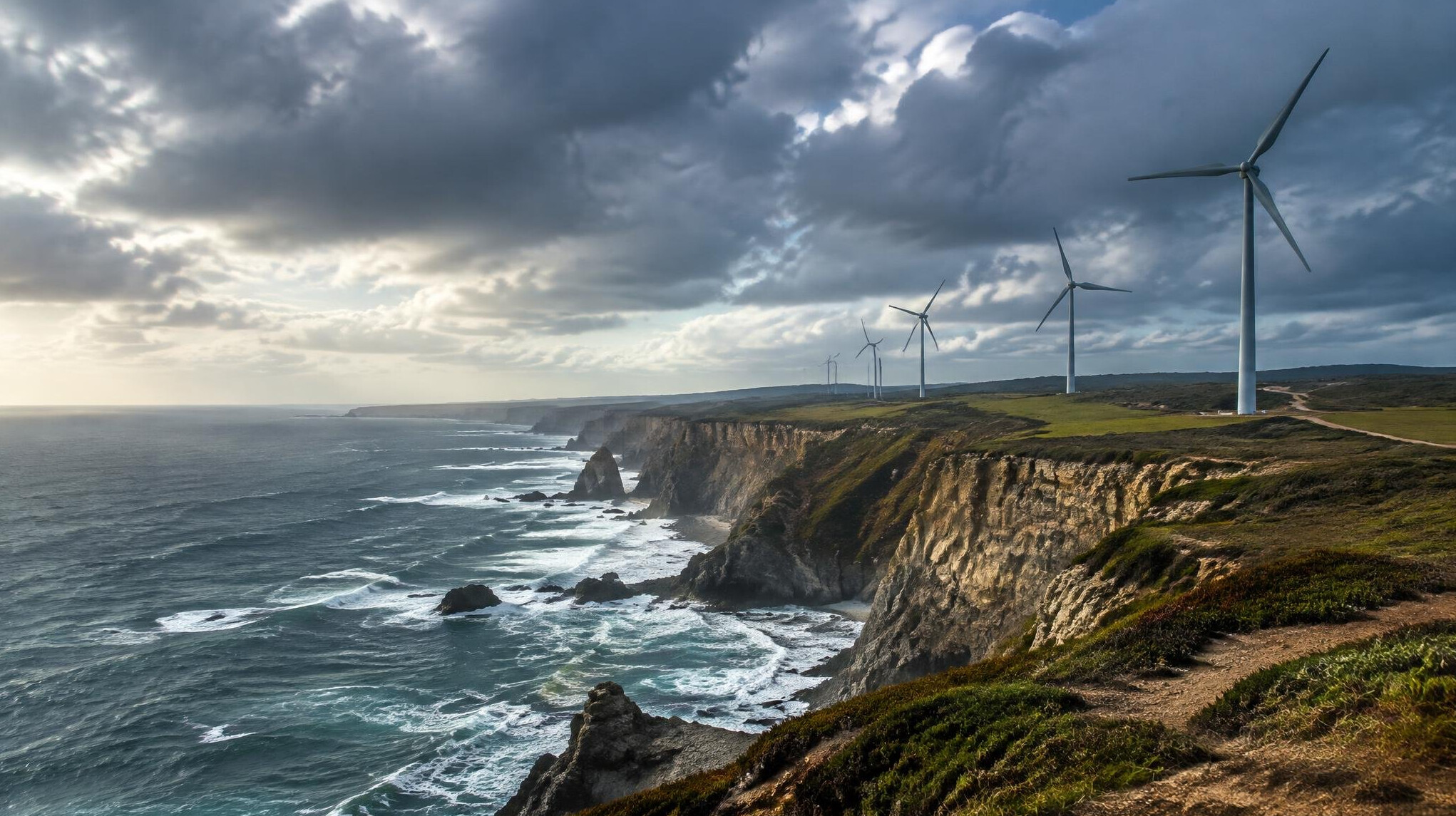 Portuguese Atlantic coastline with wind turbines and cliffs under a dramatic sky